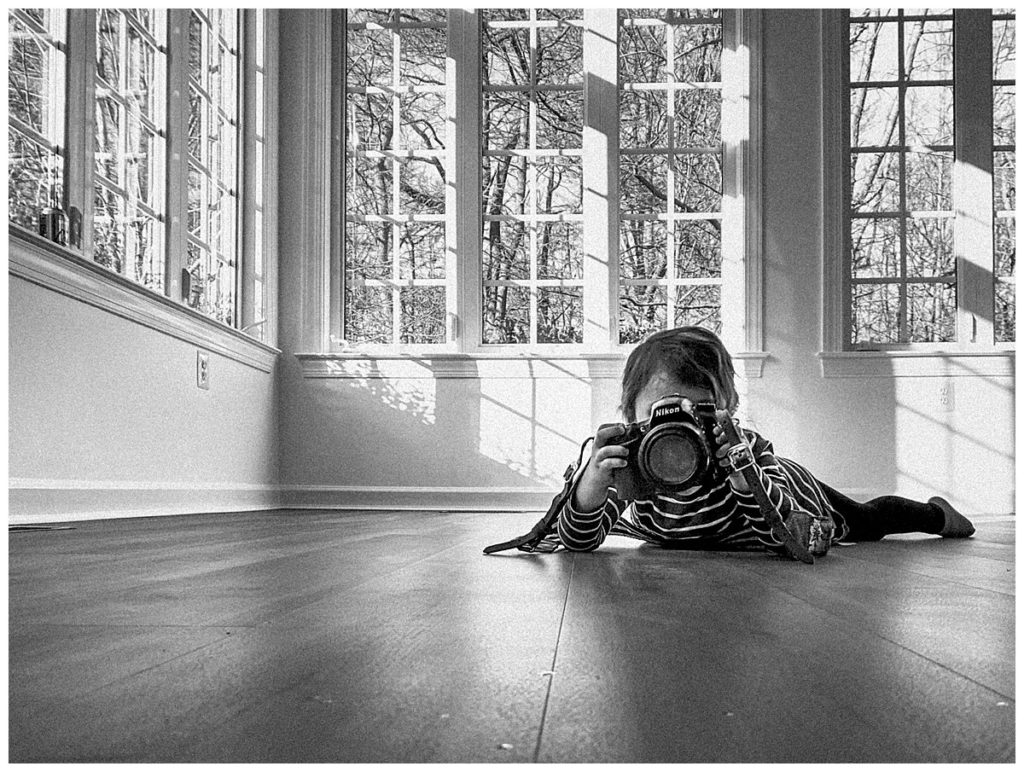 Child lying on the floor taking a picture with a Nikon camera smart phone photography tips Black and White