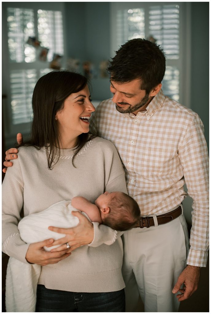 Family Portrait of a Mom and Dad holding their new son in their master bedroom during a lifestyle Indoor Newborn Photography Session on the Main Line.