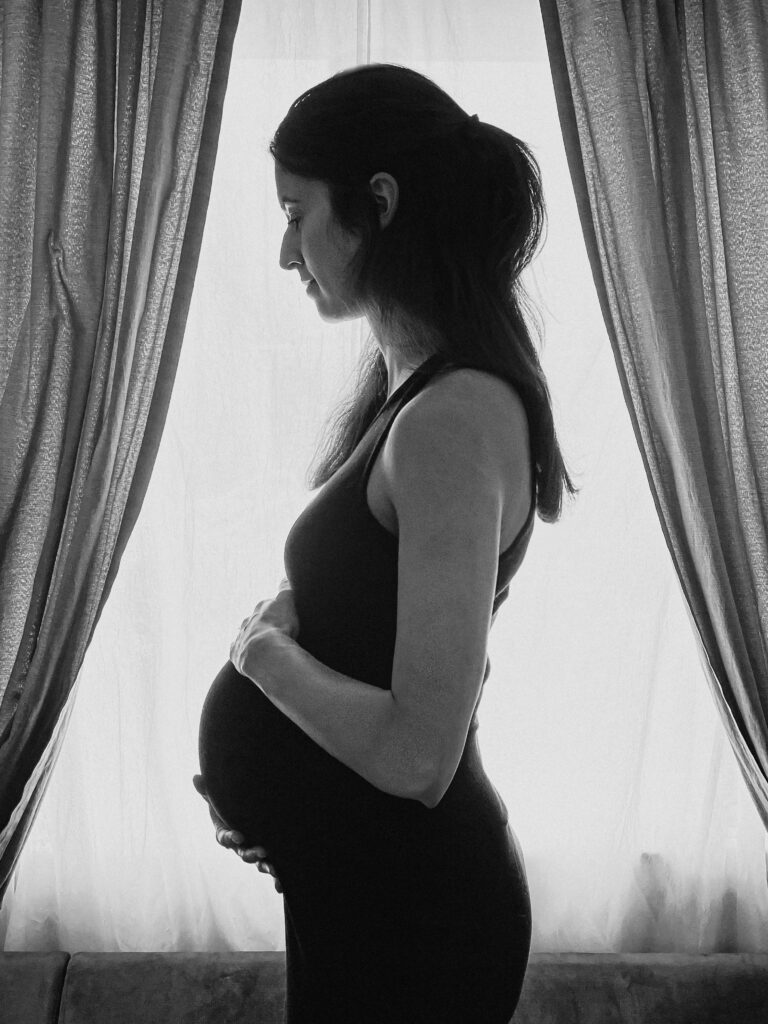 Black and White Maternity Self Portrait in front of a window.
