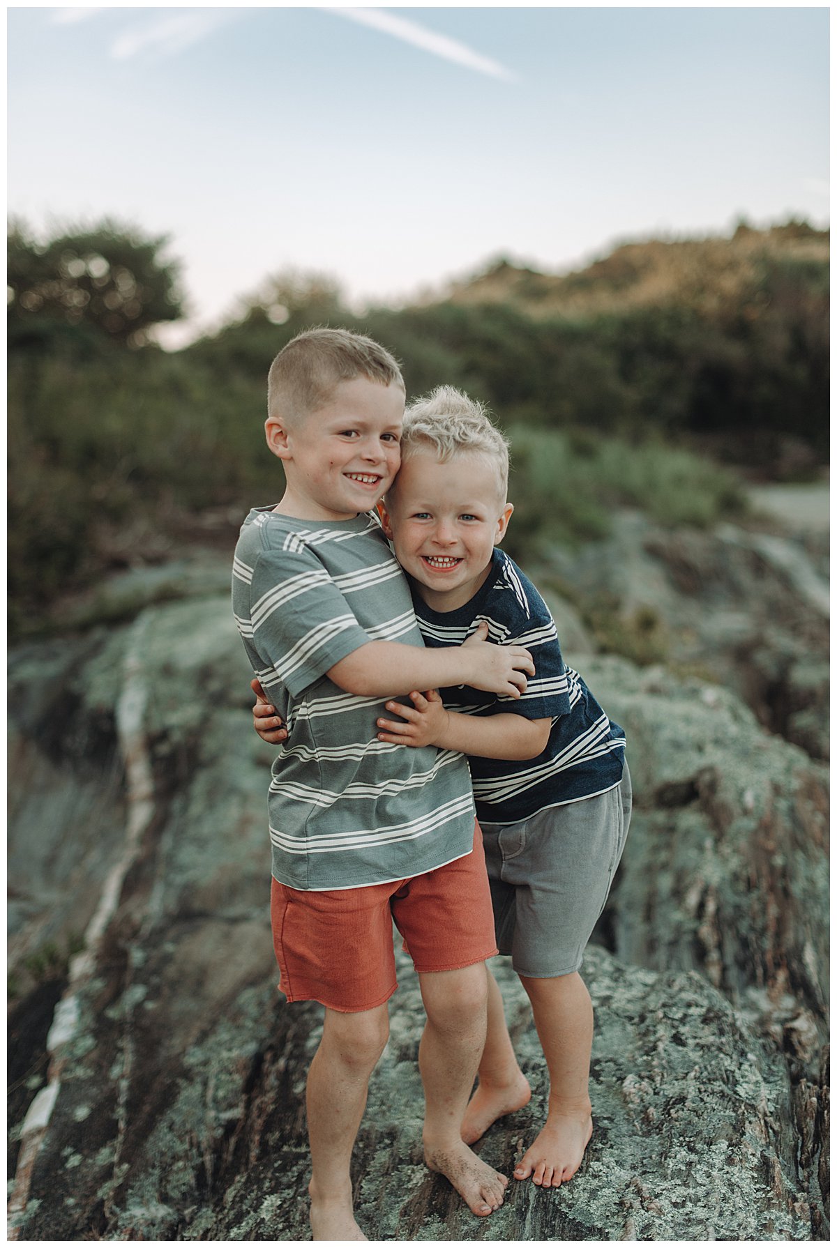 brothers hug each other and smile while standing on a rock